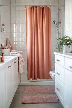 a bathroom with a pink shower curtain and rugs on the floor in front of it