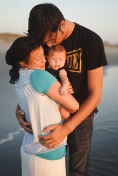 a man and woman holding a baby in their arms while standing next to the water