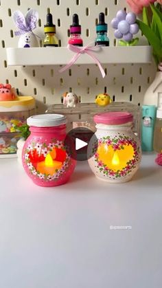 three jars with flowers on them sitting on a table next to other containers and vases