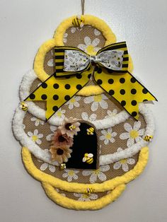 a yellow and white wall hanging decoration with flowers on the front, two bows at the top