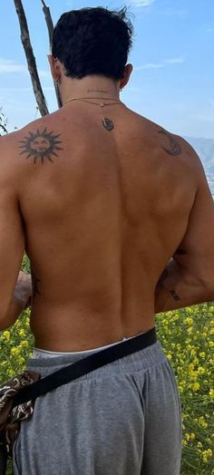 a man with tattoos on his back standing in front of flowers and looking at the sky