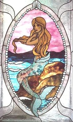 a stained glass window with a mermaid sitting on top of a rock in the ocean