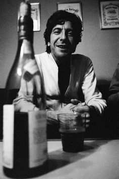 a black and white photo of a man sitting at a table next to a wine bottle