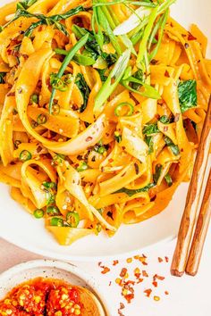 a white bowl filled with noodles and vegetables next to chopsticks on a table