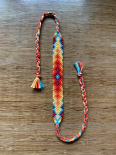 an orange, blue and red beaded lanyard with tassels on a wooden surface