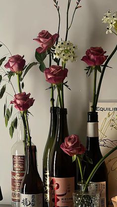 three wine bottles with flowers in them sitting on a table next to two empty glasses