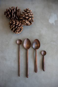 five wooden spoons and two pine cone on a table