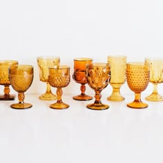 an assortment of glass goblets are lined up on a white surface, including one in the middle