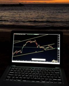 an open laptop computer sitting on top of a wooden table next to the ocean at sunset