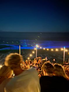 a group of people standing on top of a beach next to the ocean at night