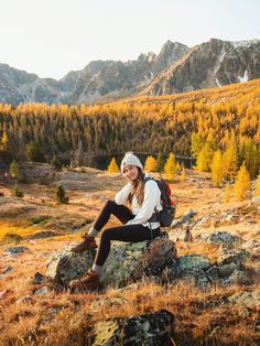 a woman sitting on top of a rock in the mountains