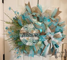 a welcome wreath hanging on the front door with blue and white ribbons around it that says welcome