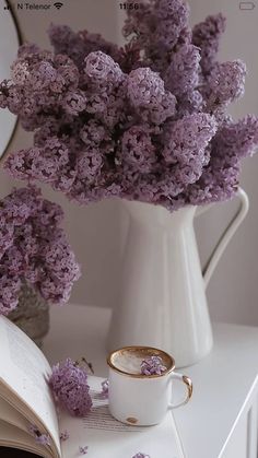 purple flowers in a white vase next to an open book