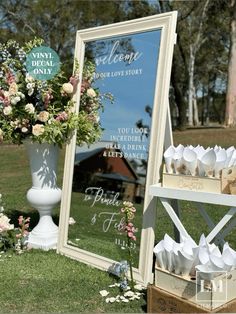 there is a mirror and some flowers on the grass near a sign that says welcome to our love story