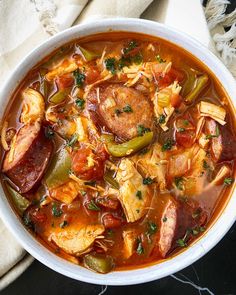 a white bowl filled with meat and vegetable soup on top of a table next to a napkin