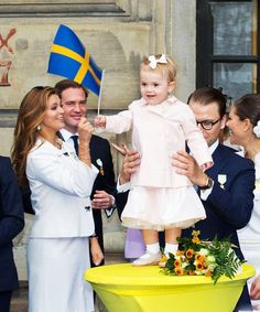 a woman holding a baby in her arms while standing next to other people and flags