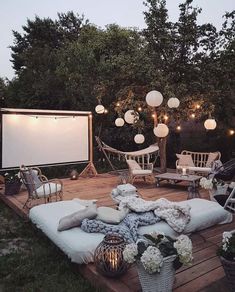 an outdoor movie screen is set up on a wooden deck surrounded by lawn furniture and string lights