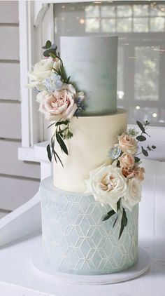 a three tiered cake with flowers on it sitting on top of a white table