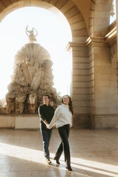 a man and woman holding hands in front of a statue