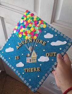 someone is holding up a blue graduation cap that says adventure is out there with balloons on it