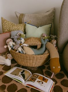 a basket filled with stuffed animals sitting on top of a bed next to a book