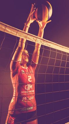 a female volleyball player is reaching up to hit the ball in front of the net