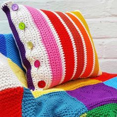 a multicolored crocheted pillow sitting on top of a couch next to a white brick wall