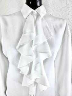 This white unlined ruffled blouse has pearl coloured button front closure, and button closure on cuffs. Some of the colouring on buttons have chipped off.  Bust-44 inches  Waist-42 inches  Shoulder to Shoulder across back- 20 inches  Shoulder to hem- front- 24 inches  Underarm to sleeve end- 14.5 Black Formal Gown, Flying Tomato Dress, White Ruffle Blouse, Ruffled Blouse, Womens Blouses, Tuxedo Jacket, Ruffled Collar, Pearl Color, Formal Gowns