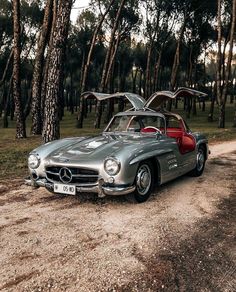 an old mercedes sports car is parked on the side of a dirt road in front of some trees