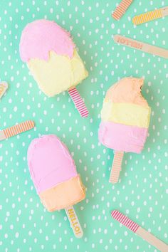 three popsicles with different colored frosting sitting on top of a blue and white polka dot tablecloth