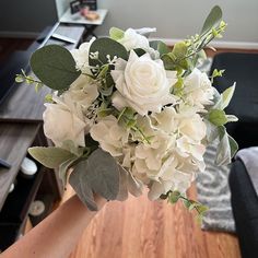 a person holding a bouquet of white flowers in their hand on top of a wooden table