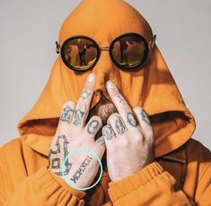 a man in a yellow hoodie with tattoos on his arms and fingers covering his face