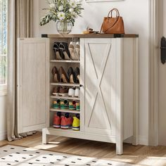 a white cabinet with shoes and purses in it next to a vase filled with flowers