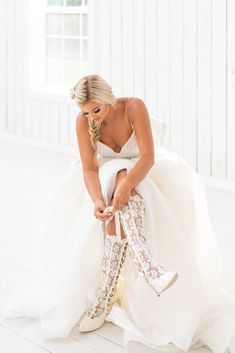 a woman sitting on top of a white chair wearing high heel boots and a wedding dress