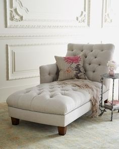 a chaise lounge chair in a white room with a table and vase on the floor