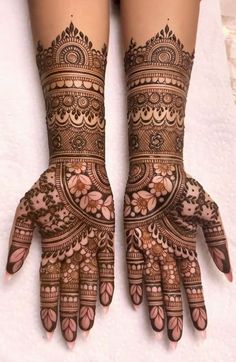 two hands with henna tattoos on them, one is showing the intricate design and the other has flowers