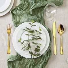 a white plate topped with green leaves next to silverware and utensils on top of a table