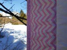 a pink and white blanket hanging from the side of a tree in front of snow covered ground