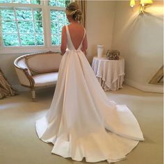 a woman standing in front of a window wearing a white wedding dress with open back