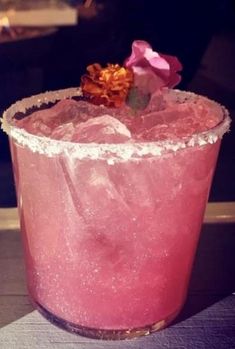 a close up of a pink drink with ice and flowers on the rim, sitting on a table