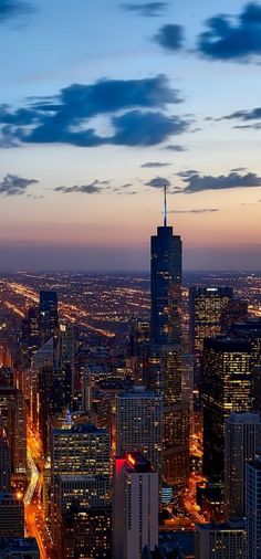 an aerial view of a city at night with skyscrapers lit up and clouds in the sky