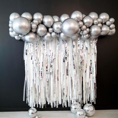 a bunch of silver balloons hanging from the side of a wall with tassels