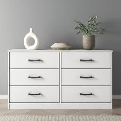 a white dresser with two vases on top and one potted plant in the middle