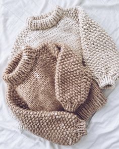 two knitted sweaters laying on top of a white bed next to each other