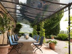 an outdoor dining area with blue chairs and tables under a pergolated roof, surrounded by greenery