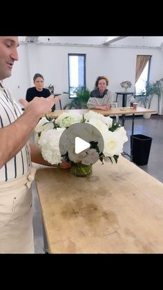 a man standing in front of a wooden table with white flowers on top of it