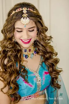 a woman with long curly hair wearing a blue dress and gold jewelry on her head