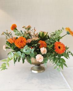 a vase filled with lots of flowers sitting on top of a white table covered in green leaves