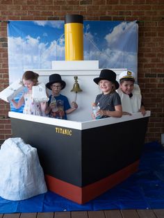 three children are sitting on a boat in front of a brick wall and blue tarp