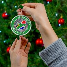 a person holding up a christmas ornament in front of a tree with ornaments